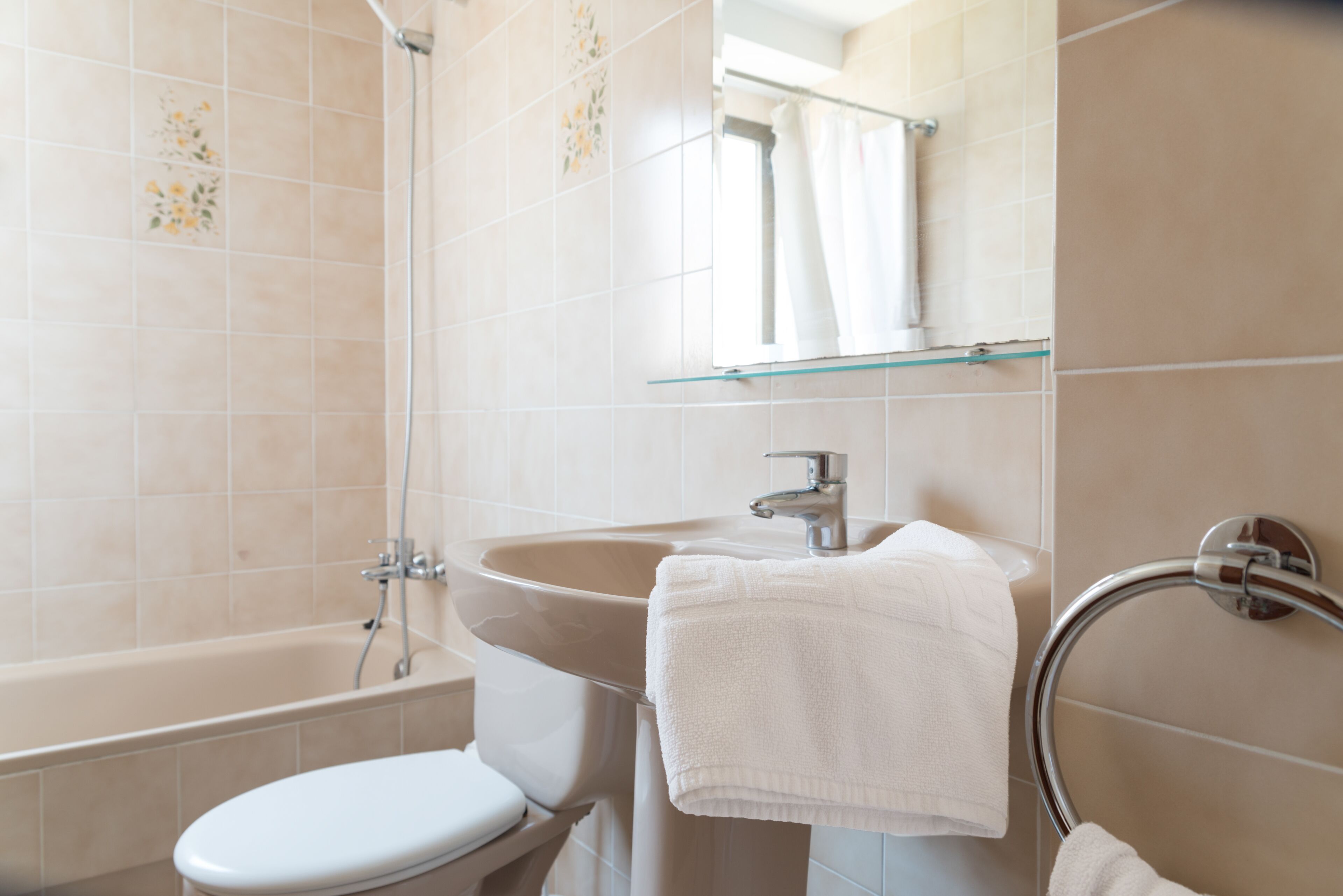 Un baño con bañera, inodoro, lavamanos y un estante de vidrio sobre el lavamanos.