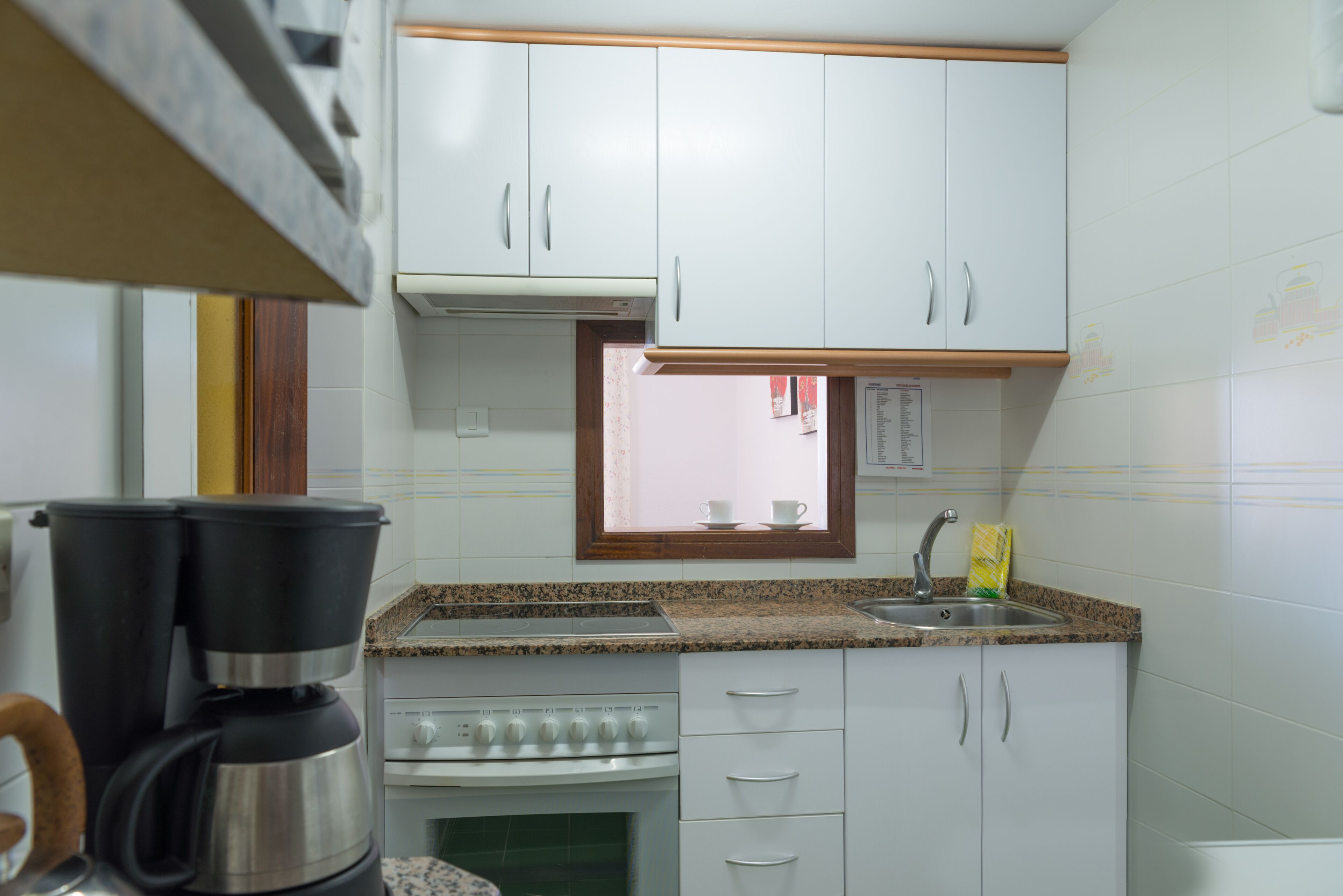 A kitchen with white cabinets, a granite countertop, a built-in oven, and a coffee maker.