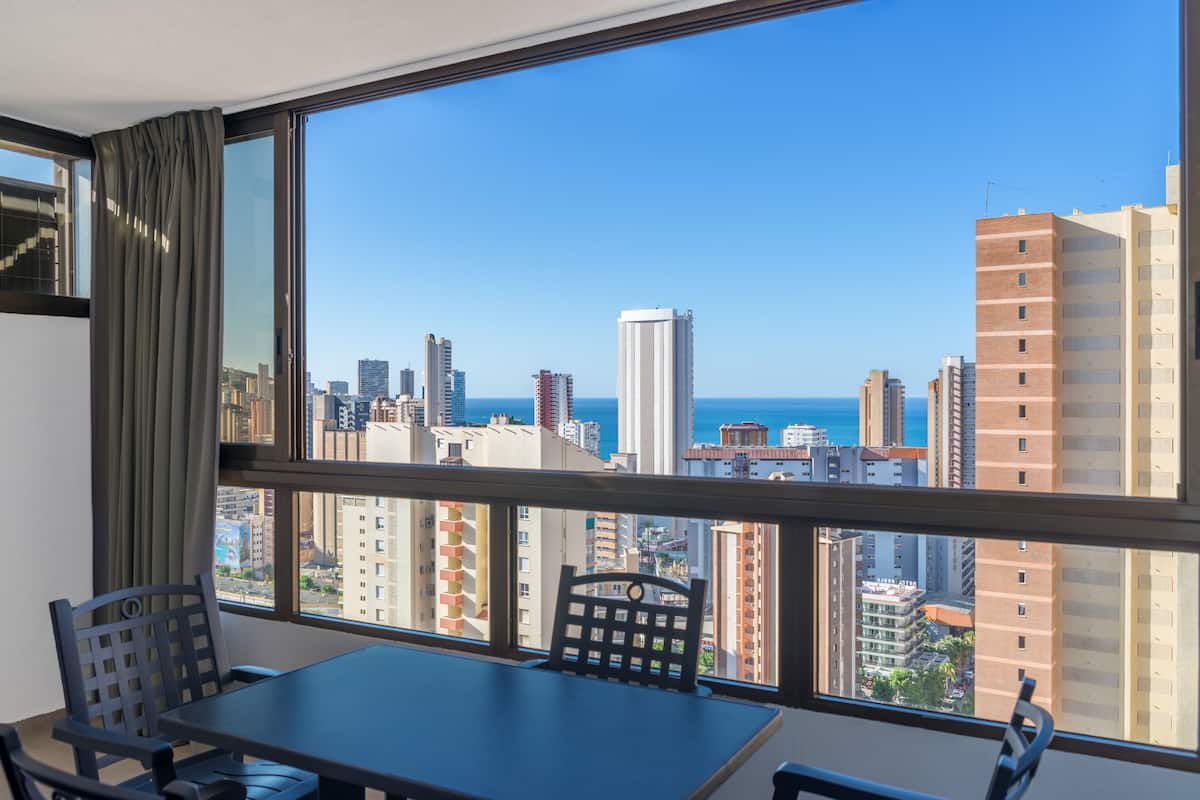 A room with a large window overlooking a cityscape and the sea.