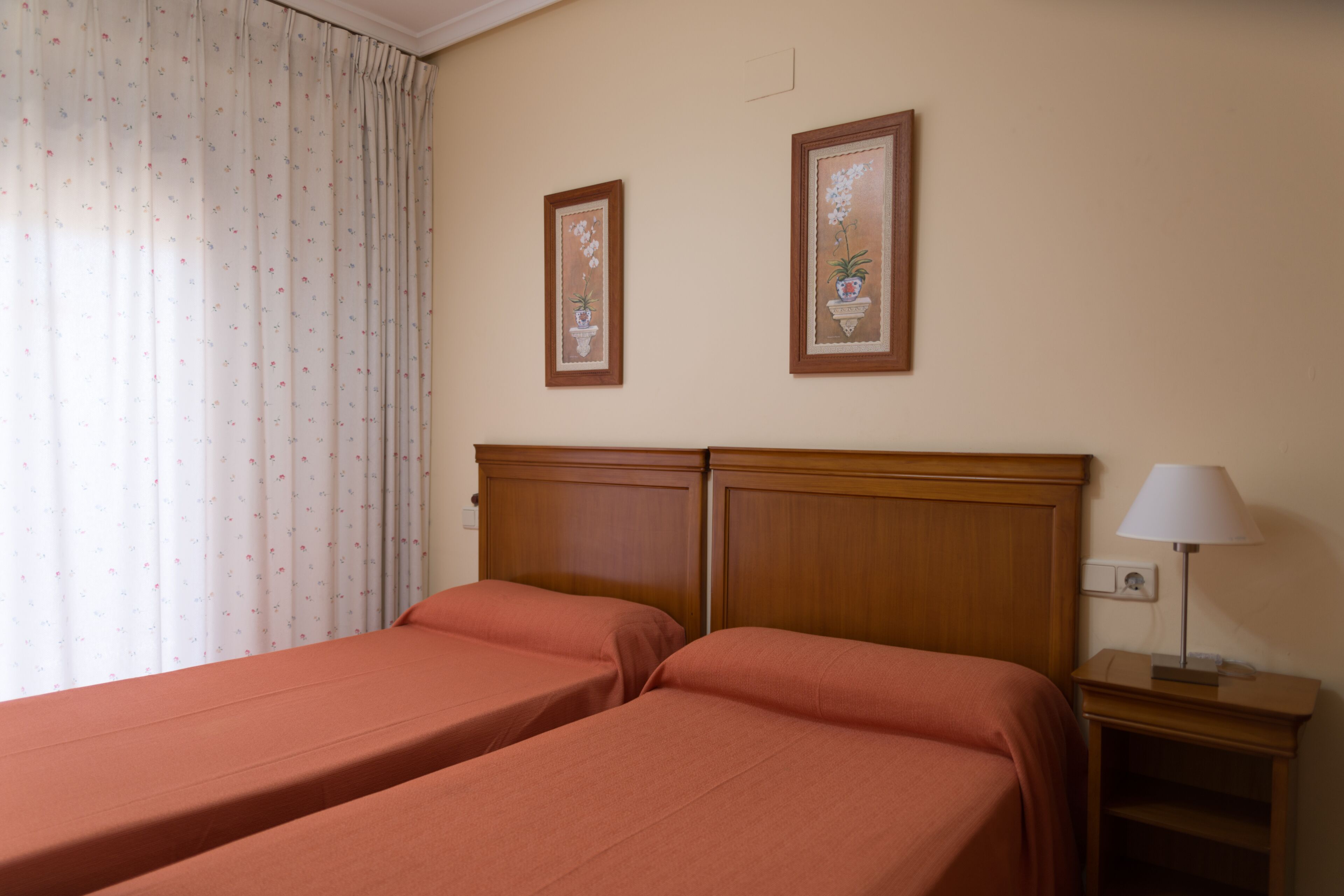 A hotel room with two beds, a nightstand with a lamp, and two framed pictures on the wall.