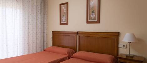 A hotel room with two beds, a nightstand with a lamp, and two framed pictures on the wall.