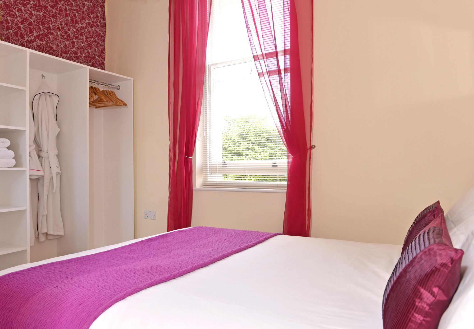 A bedroom with a bed, a wardrobe, and a window with curtains.
