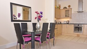 A dining area with a glass table and black chairs, a vase with flowers, and a kitchen in the background. - Cavendish Apartment (Eastbourne)