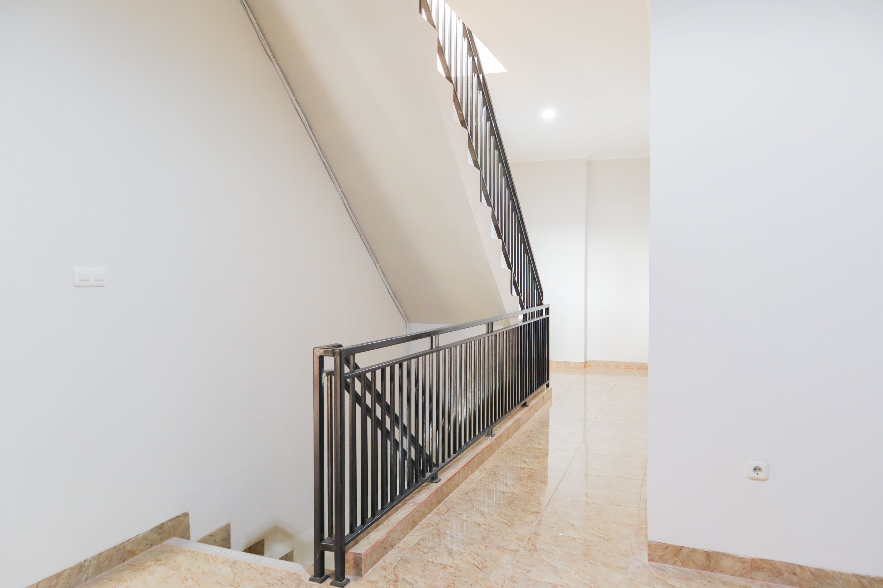 Una escalera con barandilla de metal negro, paredes blancas y suelo de mármol.