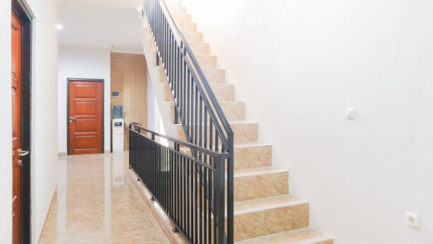 Una escalera con barandilla negra, una puerta de madera al final e un pared con diseño en el fondo.