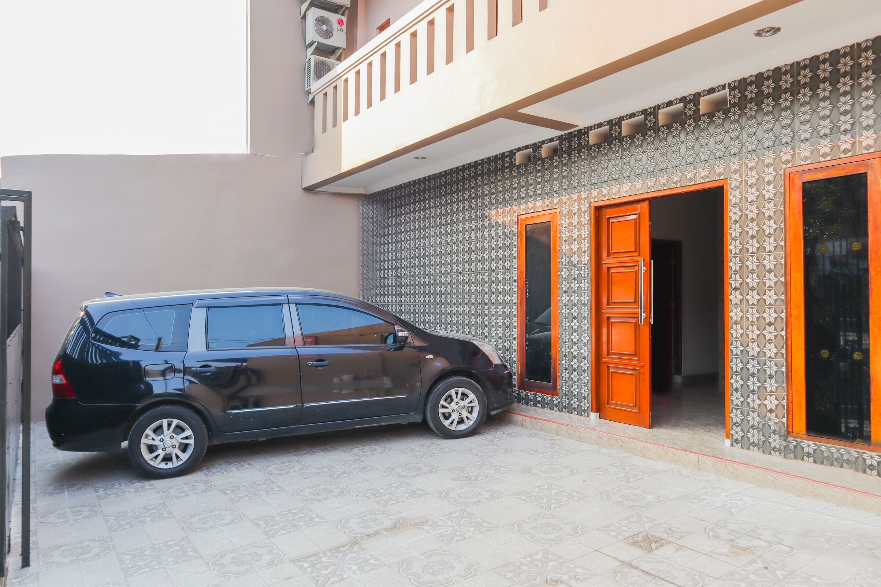 Um carro preto estacionado em frente a um edifício com paredes de azulejos estampados e duas portas de madeira.