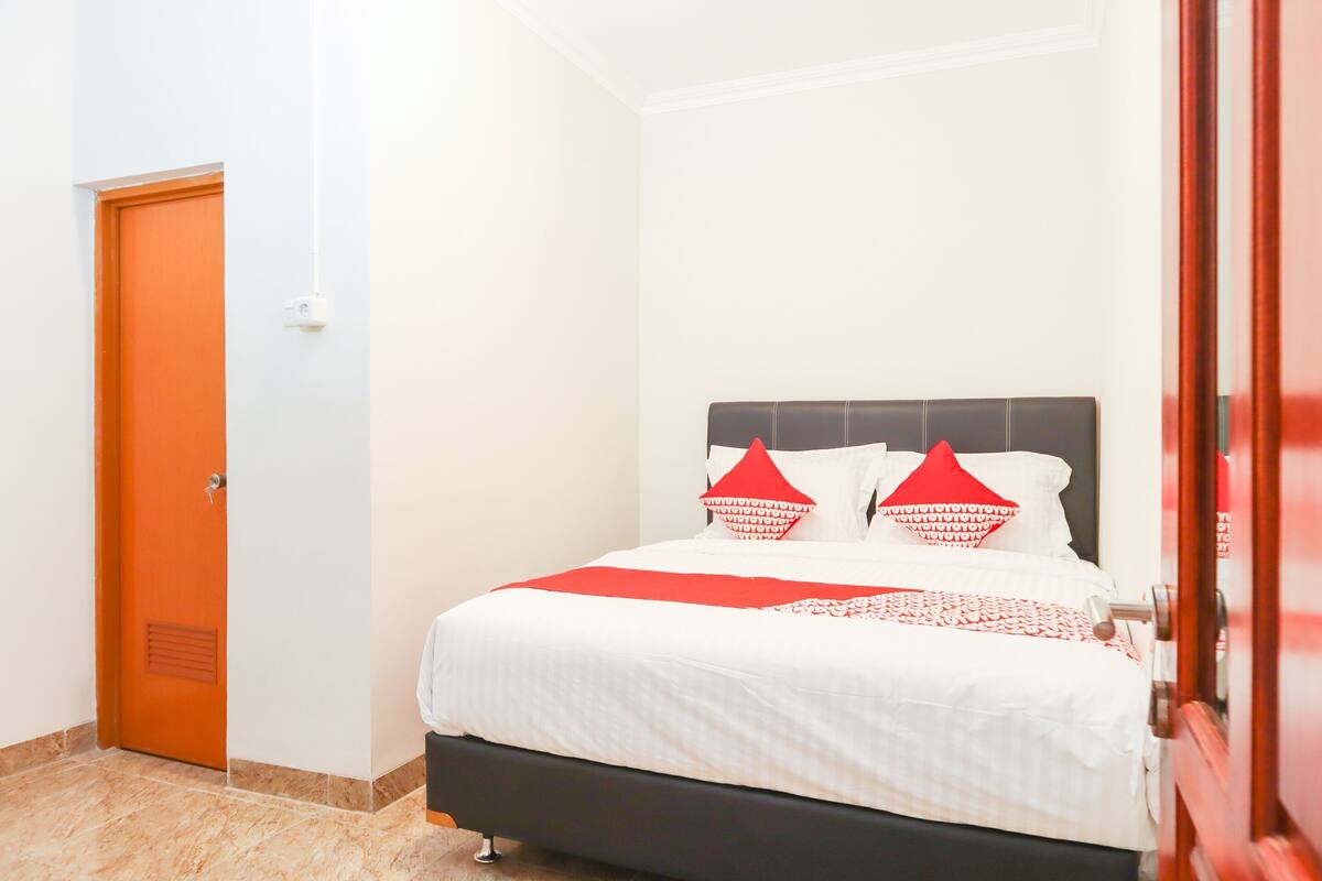 Een kamer met een bed, een deur en een lichtschakelaar aan de muur.