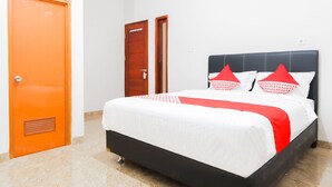 Una cama bien hecha con un cabecero negro y almohadas rojas y blancas, una puerta de madera y una pared blanca.