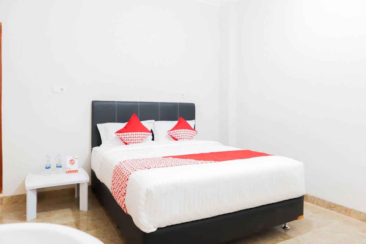 Een keurig opgeruimde hotelkamer met een bed, een klein nachtkastje en een witte muur.