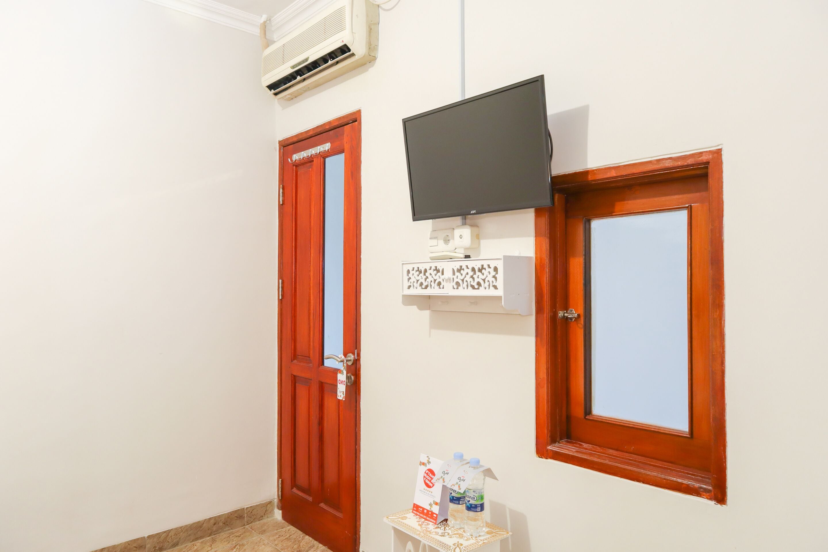 Un pasillo con dos puertas de madera, un televisor de pantalla plana montado y una pequeña mesa con agua embotellada y una tarjeta.