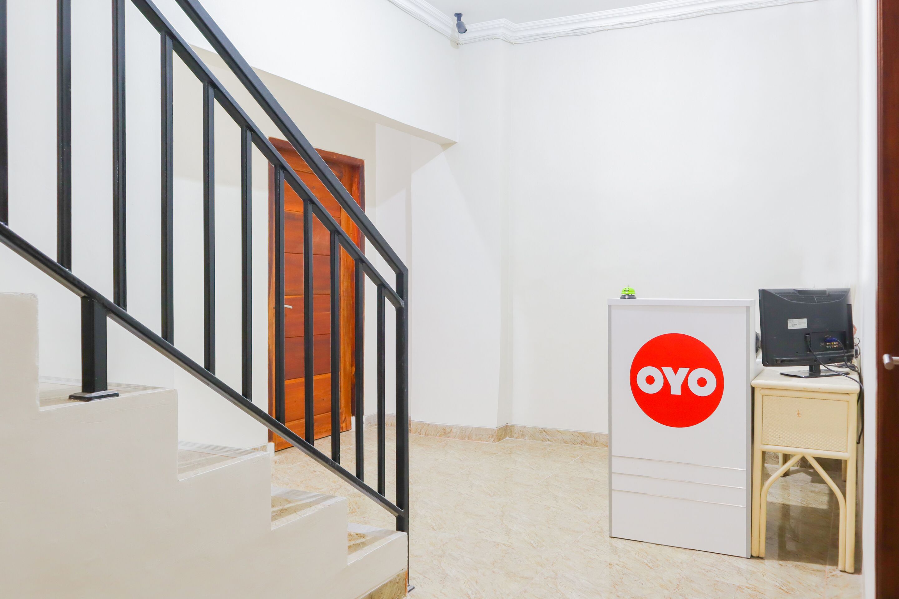 Una escalera con barandas negras que lleva a una puerta, una pared blanca y un escritorio con una computadora y el logotipo rojo de OYO.