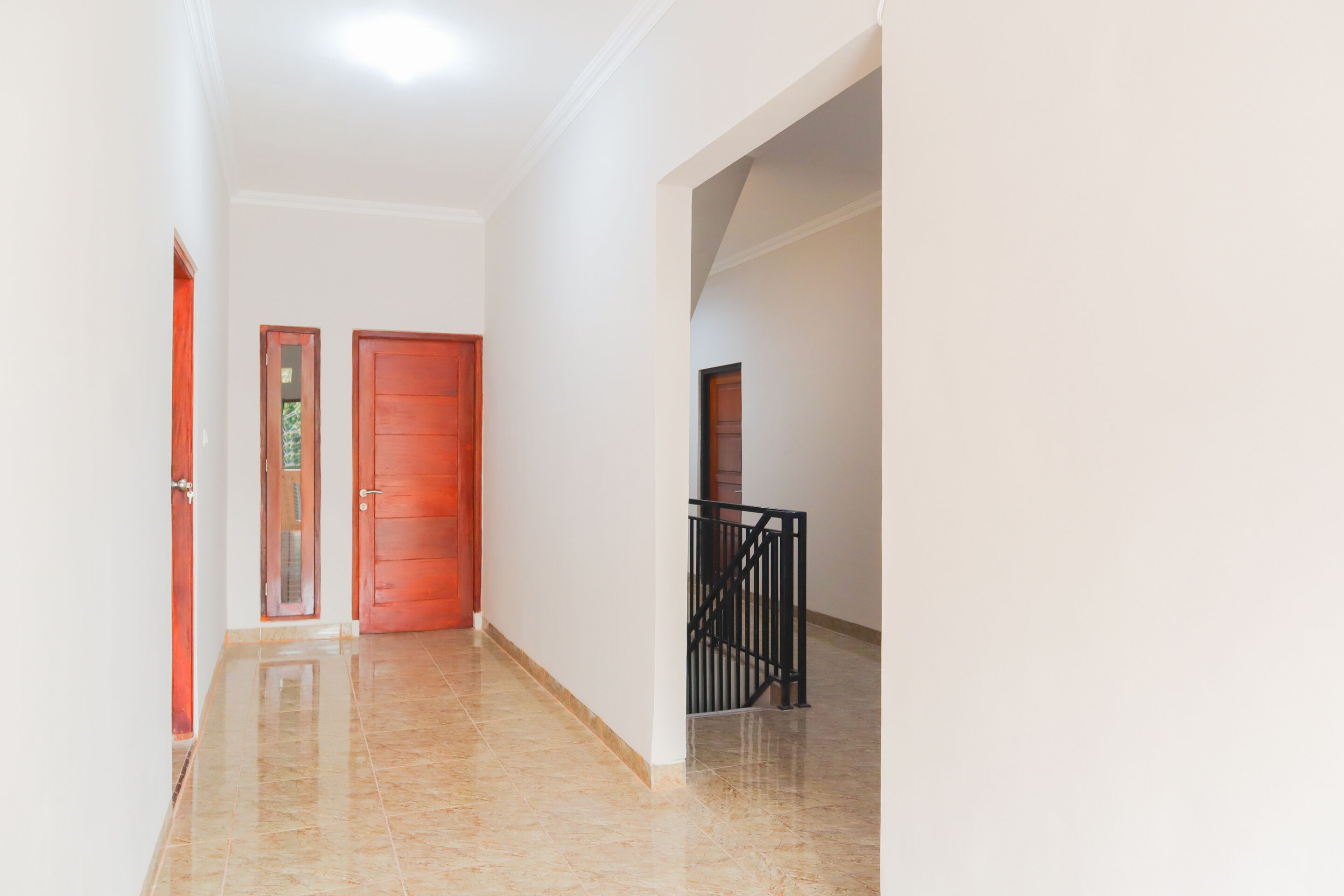 Un corridoio con due porte in legno, una ringhiera nera e un pavimento piastrellato.