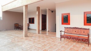Un patio abierto con piso de baldosas, un banco de madera y una puerta que da a un espacio interior.