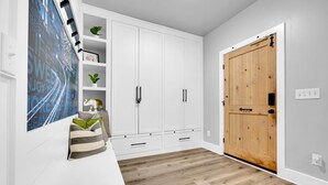 Un intérieur moderne avec des meubles blancs, une porte en bois et une œuvre d’art abstraite bleue accrochée au mur.