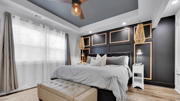 Une chambre à coucher moderne avec un grand lit, un ventilateur de plafond en bois et une table de chevet avec une lampe.