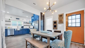 Une cuisine moderne avec des meubles bleus, un coin repas avec une table en bois et des chaises à motifs, et un panneau « Il est interdit de fumer » sur la porte.