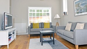 Een moderne woonkamer met een grijze bank, een salontafel, een tv op een meubel en een raam met zonwering.