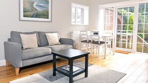 Een woonkamer met een grijze bank, een zwarte salontafel en een eethoek met witte stoelen.
