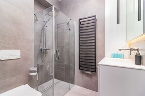Casa de banho moderna com cabine de chuveiro em vidro, porta-toalhas e lavatório branco com artigos de higiene pessoal.