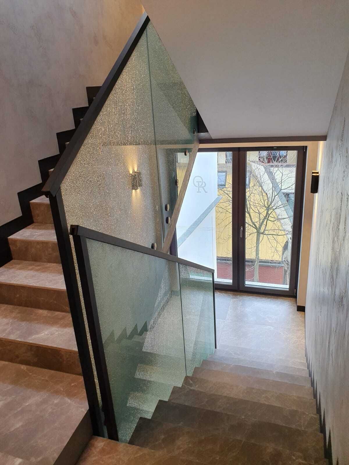Un escalier moderne avec des rampes en verre et une vue sur l’extérieur.
