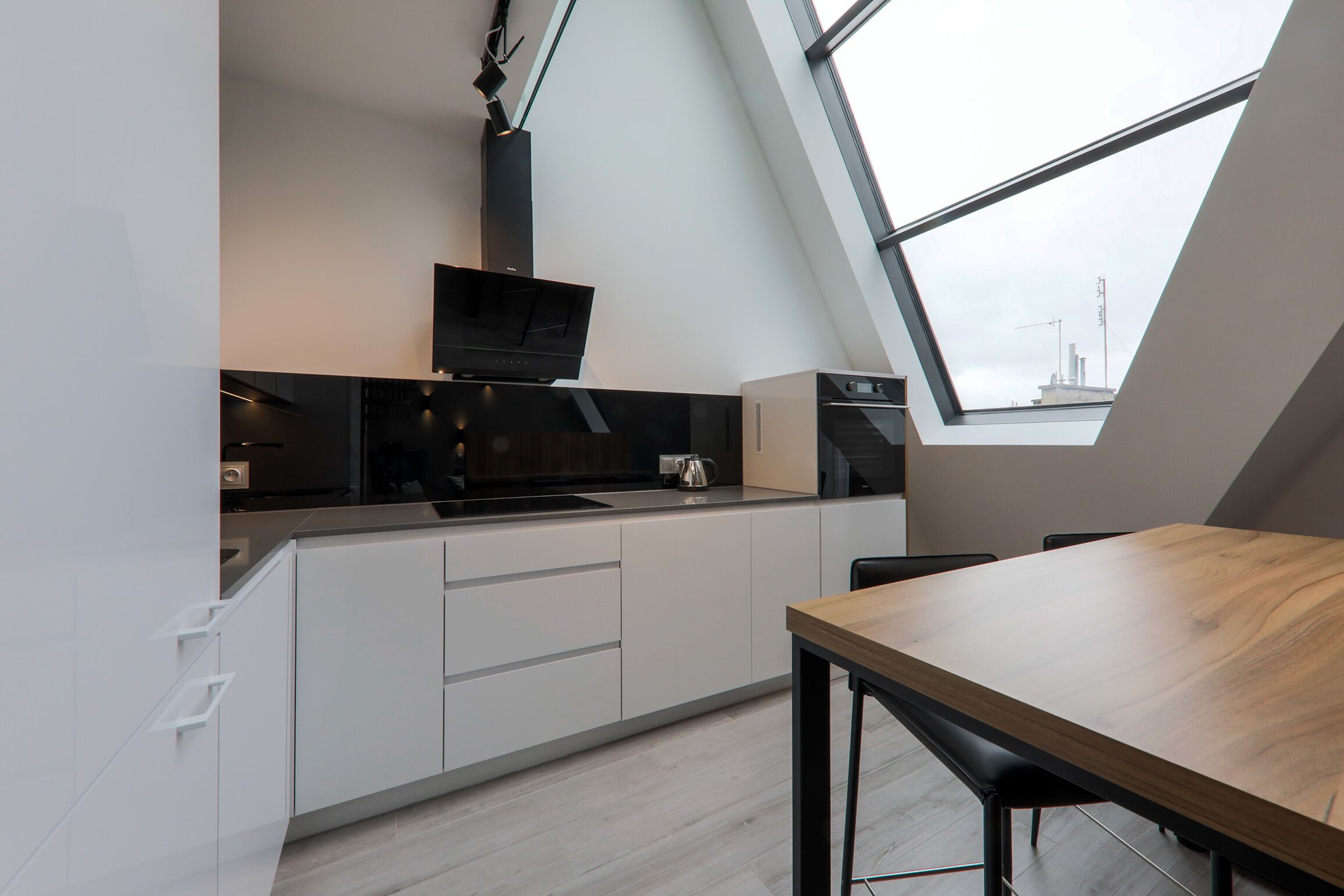 A modern kitchen with white cabinetry, a wooden dining table, and a skylight.