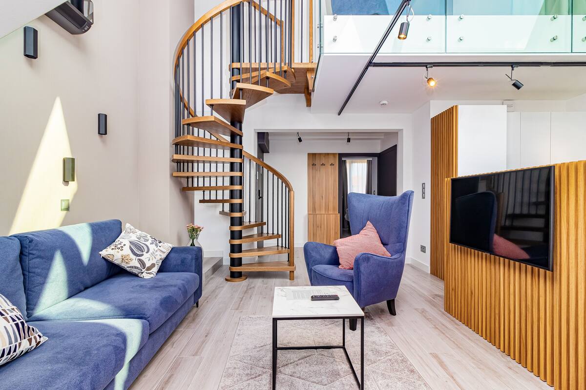 Een moderne woonkamer met een spiltrap, een blauwe bank, een blauwe fauteuil, een flatscreen televisie en een houten accentmuur.