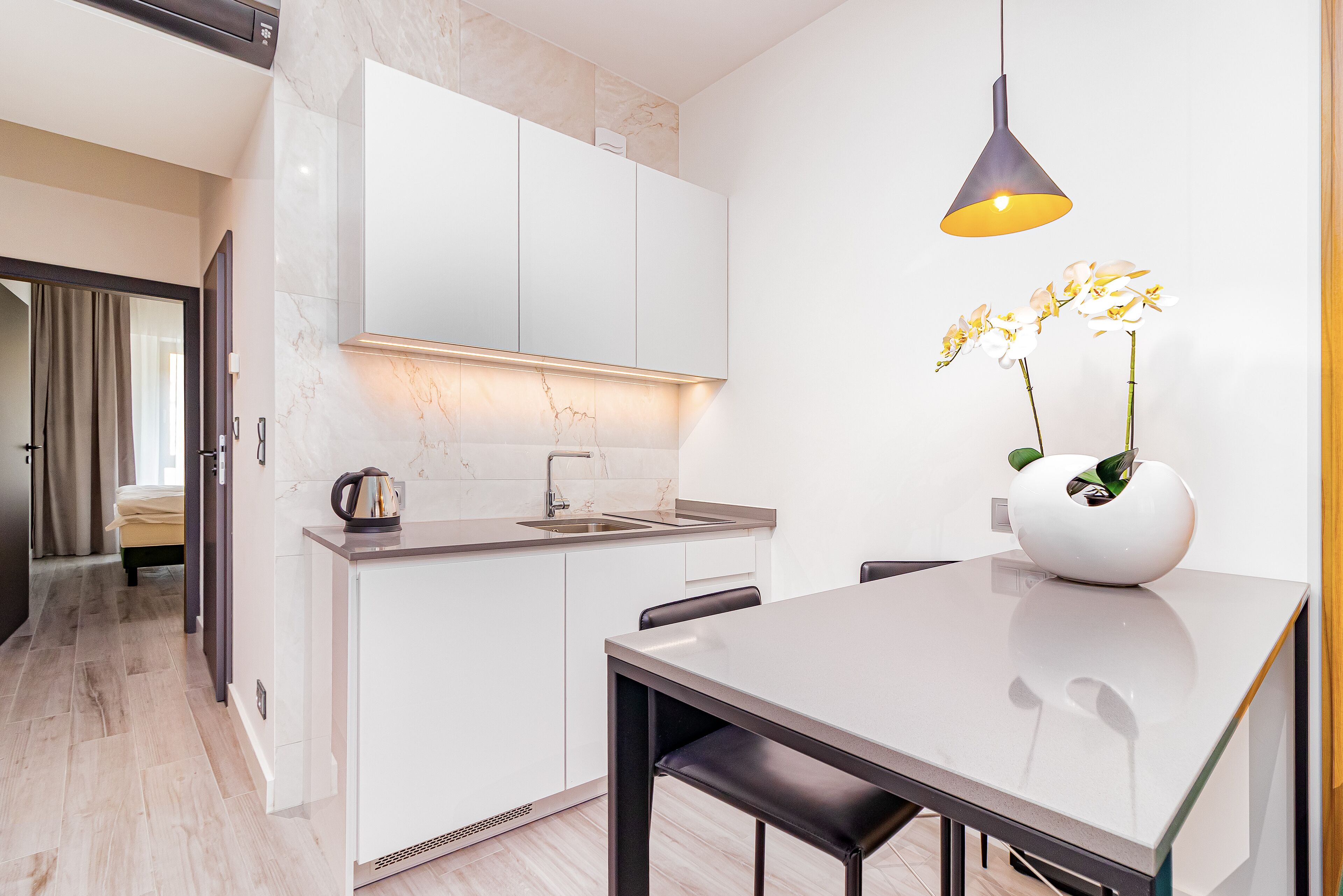 Une cuisine moderne avec des meubles blancs, un pare-feu en marbre et un coin repas comprenant une table et des chaises.