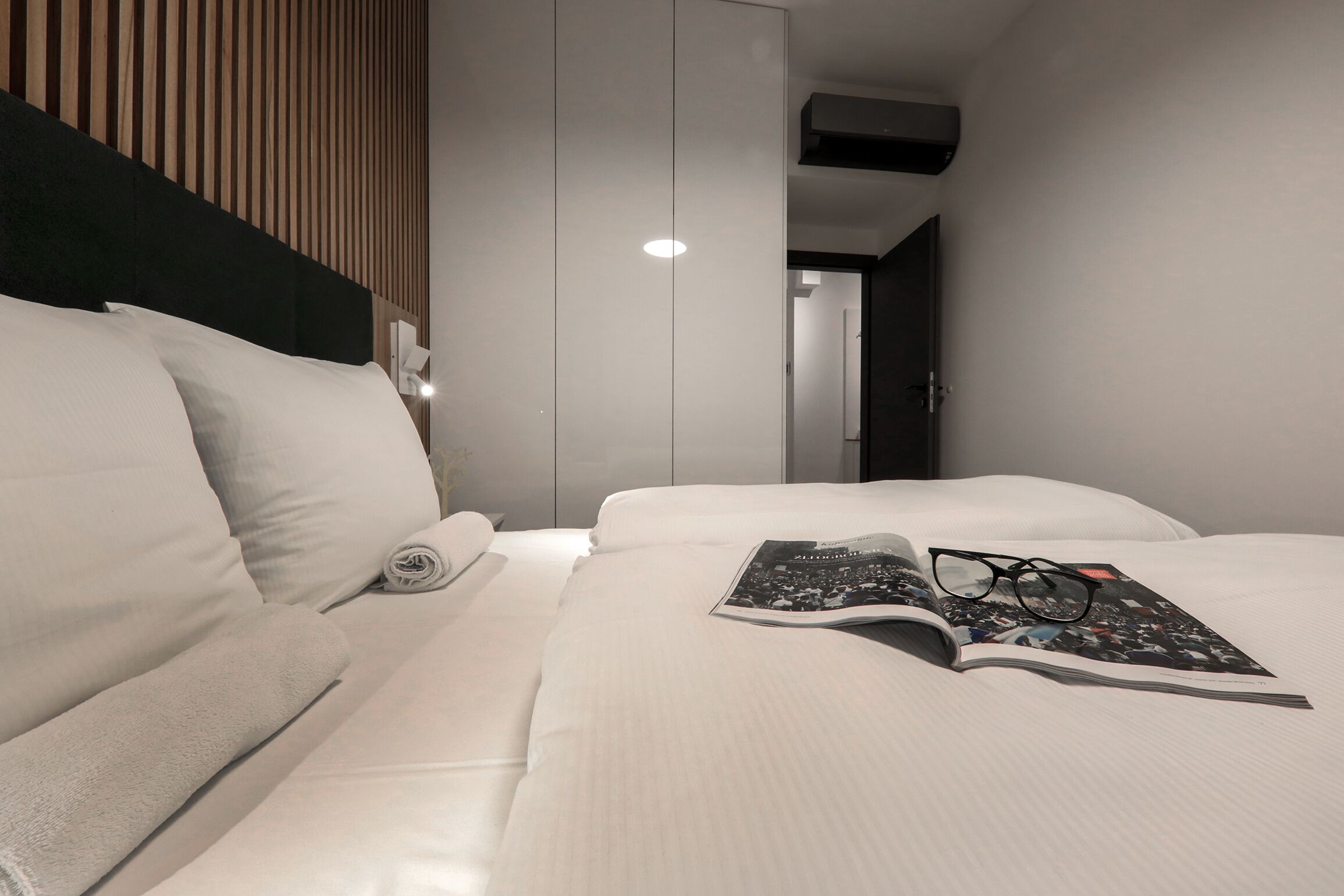 Une chambre d’hôtel moderne avec un lit bien fait, un magazine et une paire de lunettes posées sur le lit.