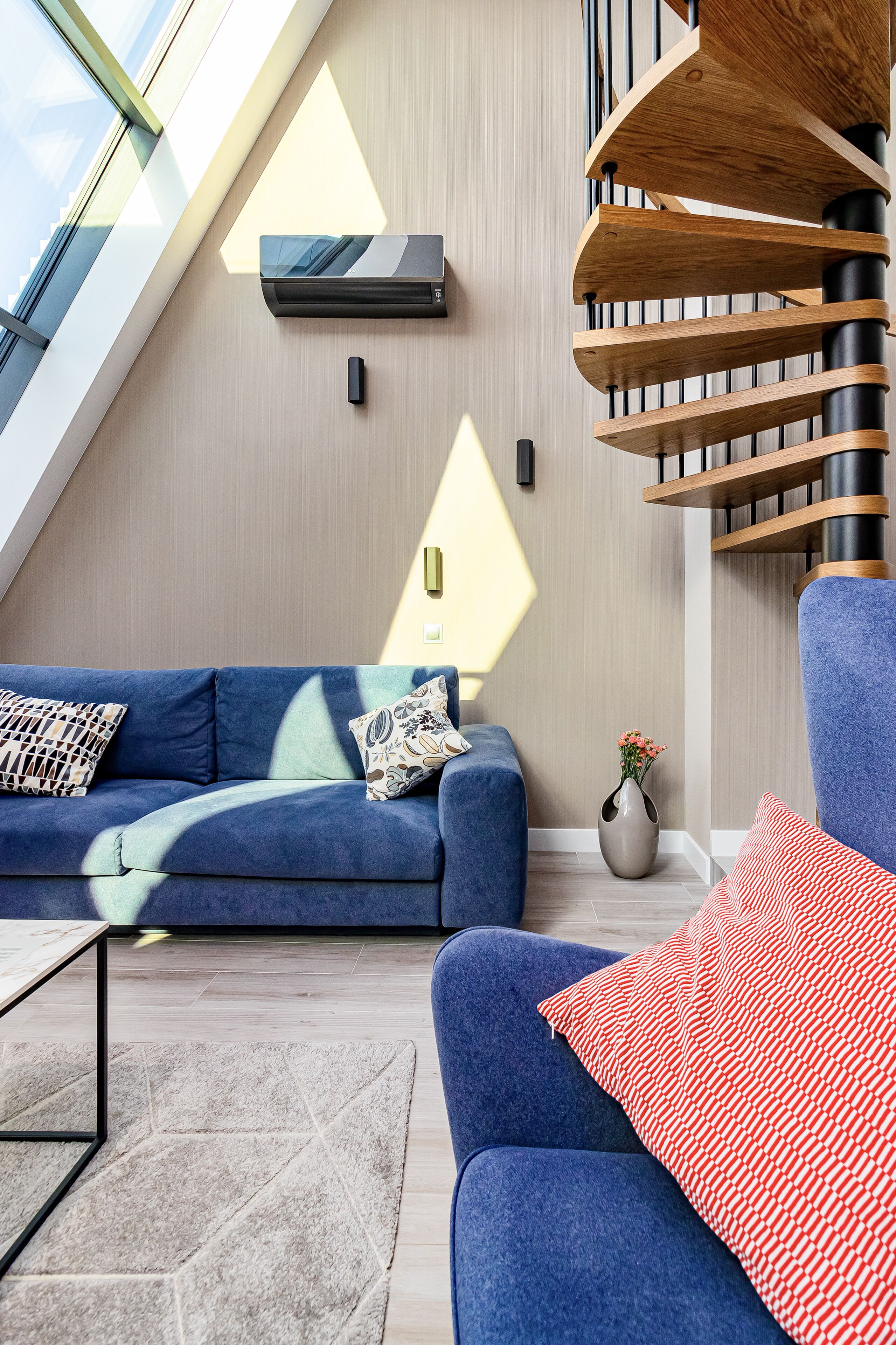 A modern living room with a blue sofa, a wooden spiral staircase, and a skylight.