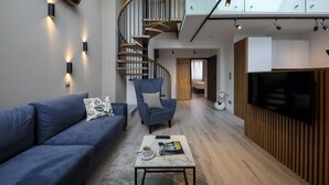 A modern living room with a blue sofa, a coffee table with a magazine, a blue armchair, and a spiral staircase. - Odrzańska Residence by Boogie Apartments (Wroclaw)