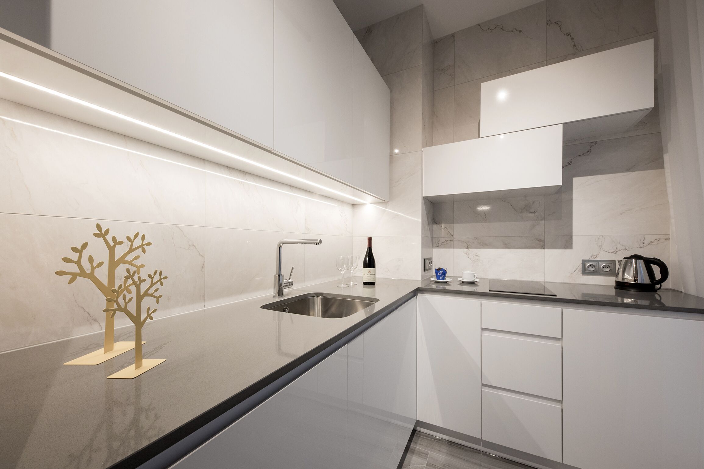 A modern kitchen with a stainless steel sink, white cabinets, and a marble backsplash.