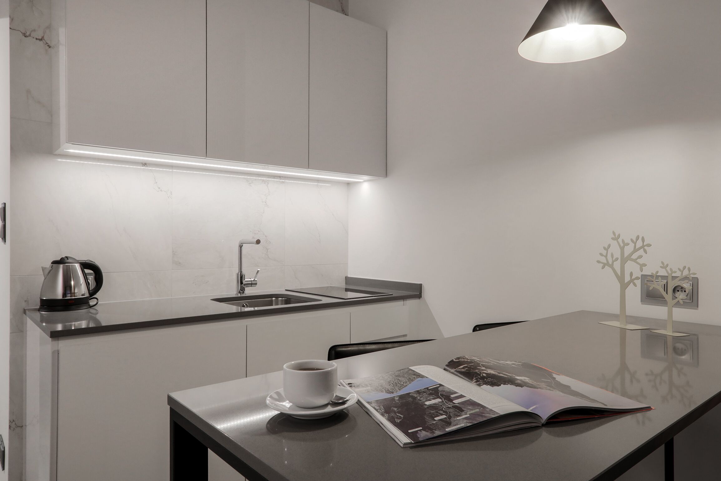 A modern kitchen with a built-in sink, a kettle, and a magazine on the counter.