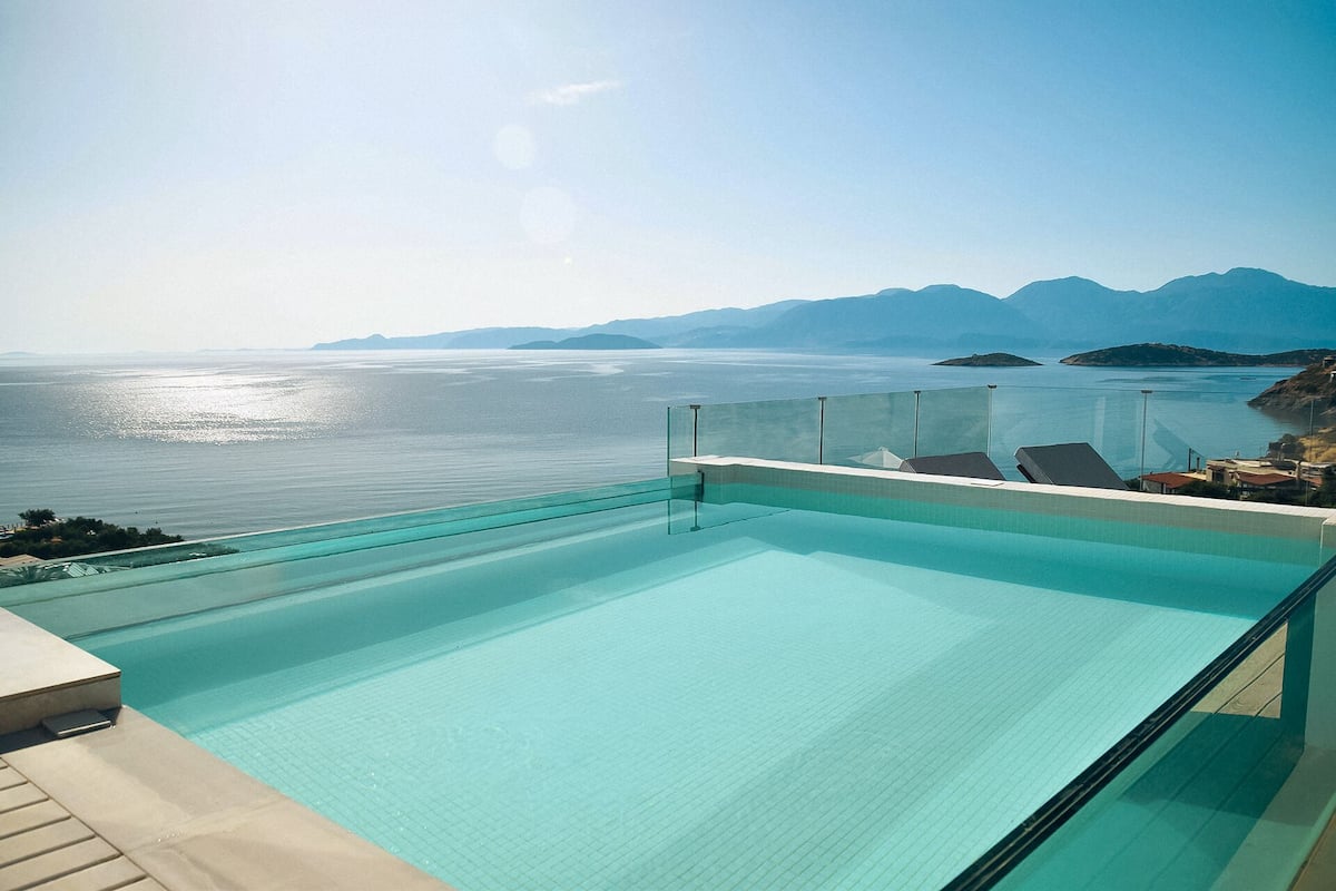 Piscina con barrera de vidrio, con vistas a una masa de agua y montañas distantes.