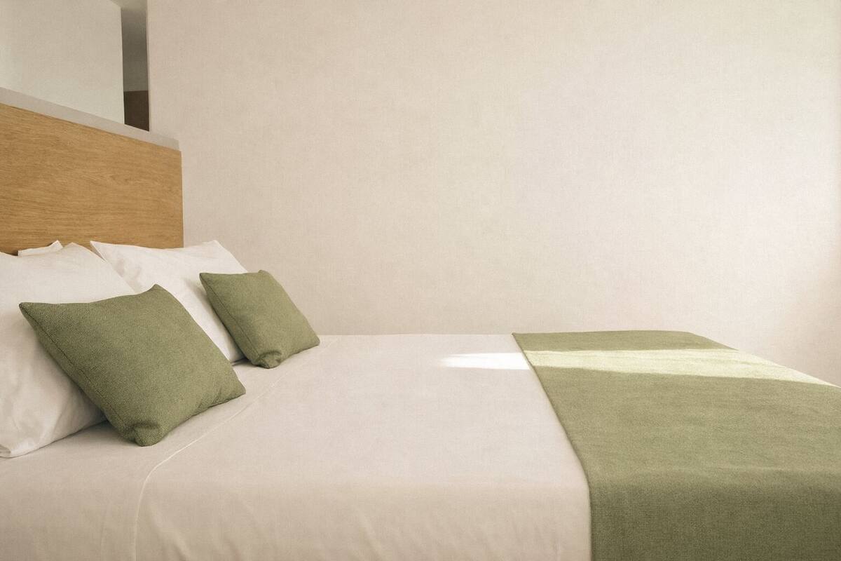 Una cama bien tendida con sábanas blancas, almohadas verdes y una manta verde de tejido de madera.