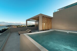 Una piscina infinita en la azotea con vistas al mar y a las montañas, un área de estar techada y una barandilla de vidrio.