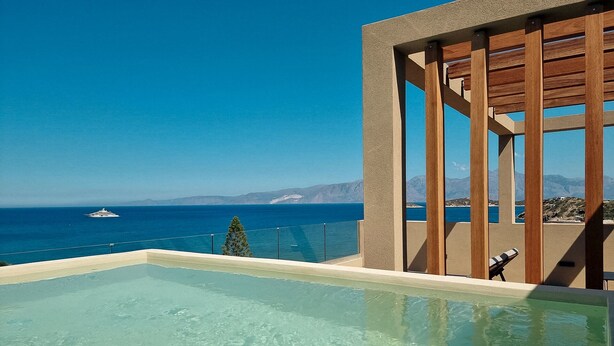 Céu azul límpido, piscina e vista para o mar com um iate ao longe.