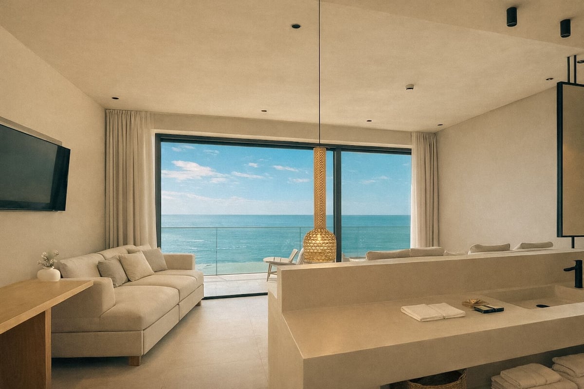 Una habitación de hotel moderna con un balcón grande, un sofá, un escritorio y un baño con un espejo amplio.