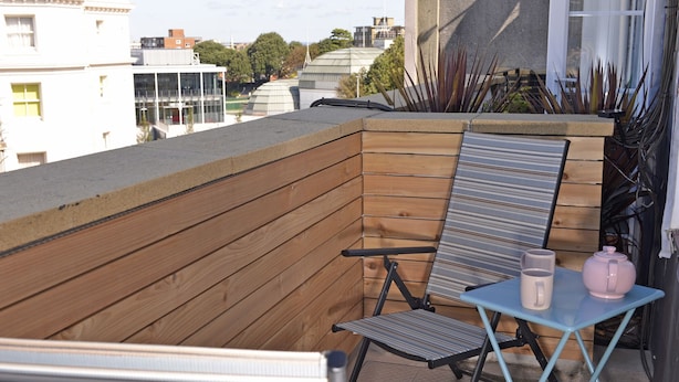 A balcony with a wooden wall, a metal chair, a small table with two mugs, and a potted plant. - Dress Circle (Eastbourne)