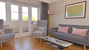 A living room with a grey sofa, a grey armchair, a coffee table with magazines, a floor lamp, and a map on the wall. - Dress Circle (Eastbourne)