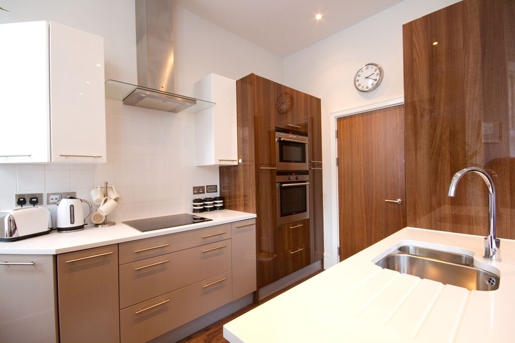 A modern kitchen with white cabinets, a stainless steel sink, and wooden accents.