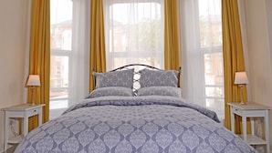 A bedroom with a bed, two bedside tables, and a window with yellow curtains.
