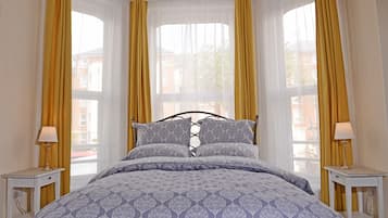 Quarto com cama, duas mesas de cabeceira e janela com cortinas amarelas.