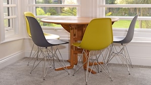 A dining area with a round wooden table and four chairs, one yellow and three gray, with metal legs.