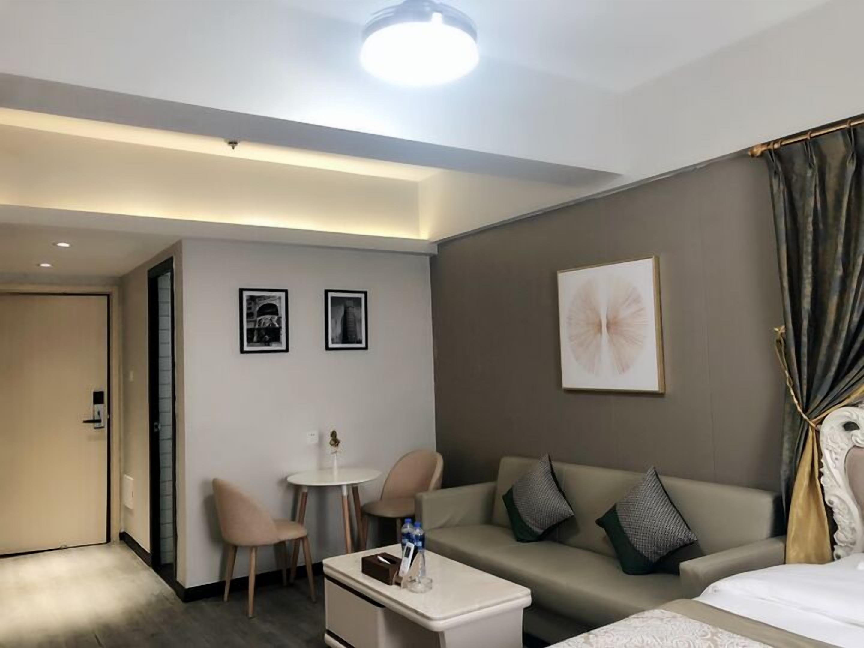 Una habitación de hotel moderna con sofá, una mesita, dos sillas, cama y una lámpara en el techo.