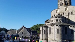 Ein historisches Steinhaus mit einem Glockenturm, umgeben von einem Parkplatz mit Autos.