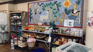 Interior de un supermercado con estantes llenos de diversos productos, una exhibición de frutas y verduras frescas, y un mural colorido en la pared.
