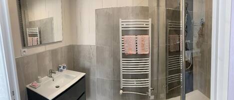 Un baño moderno con cabina de ducha de vidrio, lavabo blanco y un perchero con toallas.