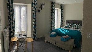 Ein Schlafzimmer mit einem Bett, einem Schreibtisch, zwei Stühlen, einem Heizkörper und Vorhängen.