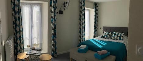 A bedroom with a bed, a desk, two chairs, a radiator, and curtains.