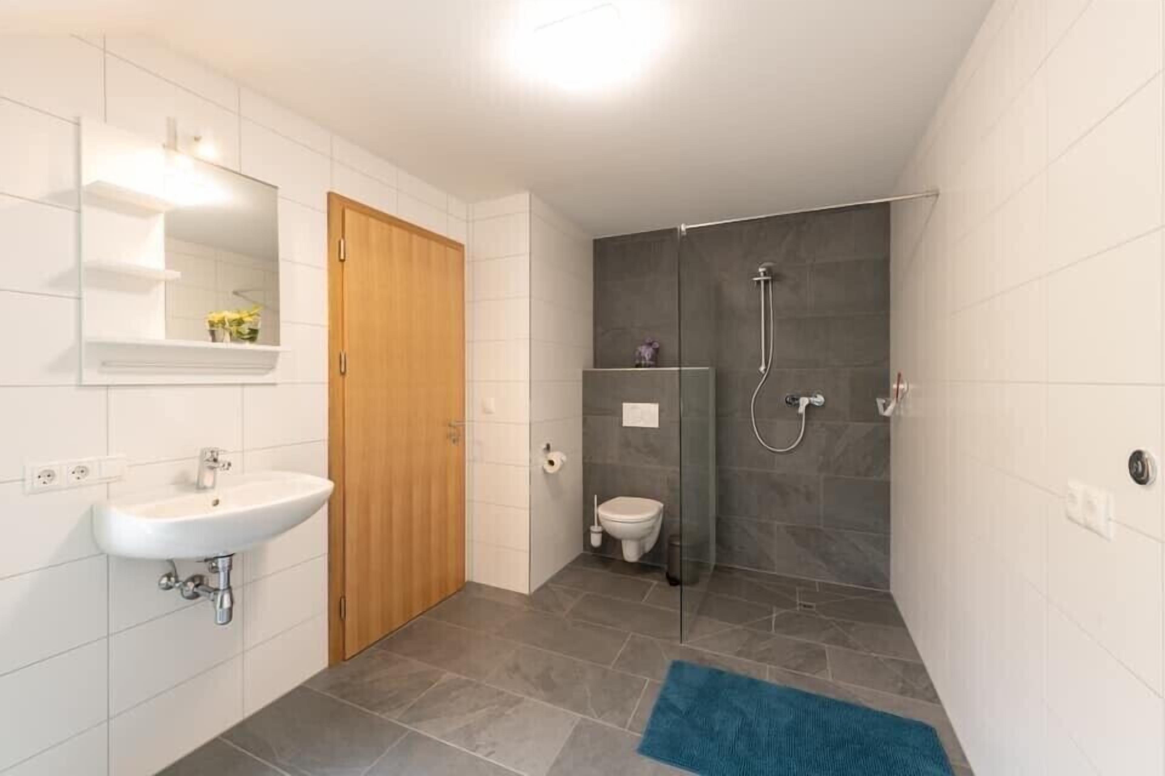 A modern bathroom with a white sink, wooden door, and a glass shower enclosure.